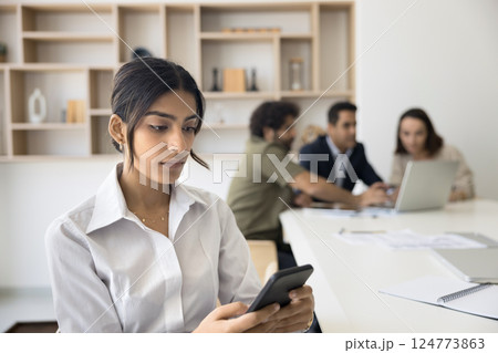 Indian office employee sitting at desk using phone 124773863
