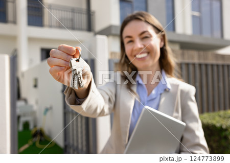Smiling real estate agent standing outdoors, holds set of keys 124773899