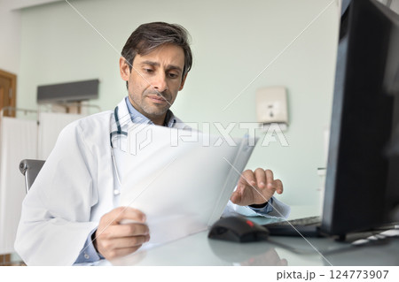 Doctor carefully reviewing documents, learning patient medical records in clinic 124773907