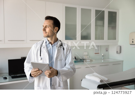 Doctor holding tablet, gazes thoughtfully into distance 124773927