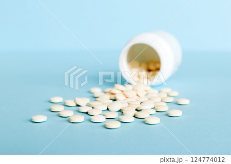 Medicine bottle and white pills spilled on a light background. Medicines and prescription pills flat lay background. White medical pills and tablets spilling out of a drug bottle 124774012