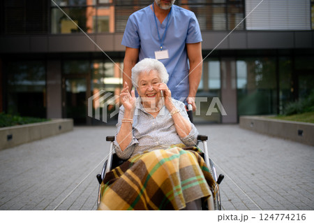 Male caregiver pushing senior woman in wheelchair. 124774216