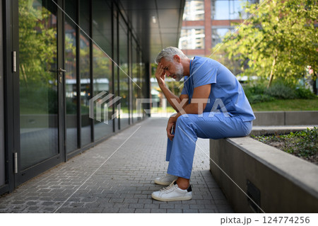 Frustrated and burnt-out doctor sitting outside the hospital, feeling down. 124774256