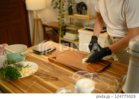 Close up of man chopping garlic on wooden cutting board in a modern kitchen 124775029