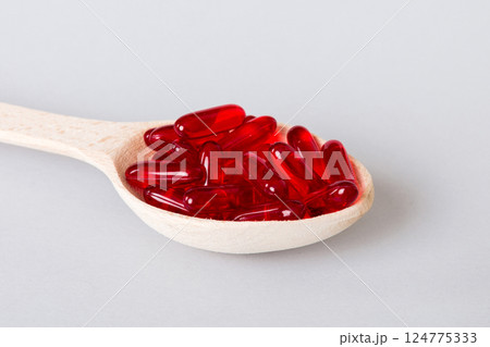 Vitamin capsules in a spoon on a colored background. Pills served as a healthy meal. Red soft gel vitamin supplement capsules on spoon Vitamin capsules in a spoon on a colored background. Pills served as a healthy meal. Red soft gel vitamin supplement capsules on spoon 124775333