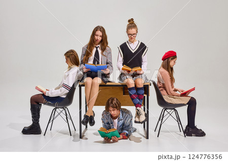 Smart, young girls, dressed stylish clothes, sitting around or on desk, and reading literature, against neutral studio background. Smart, young girls, dressed stylish clothes, sitting around or on desk, and reading literature, against neutral studio background. 124776356