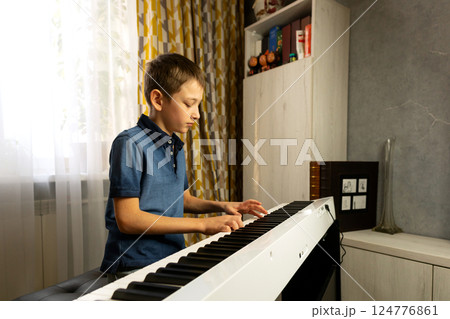 Side view of boy playing digital piano near bookshelf Side view of boy playing digital piano near bookshelf 124776861