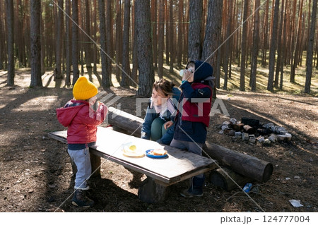 Family enjoys a picnic in the forest with children playing and eating snacks on a sunny day Family enjoys a picnic in the forest with children playing and eating snacks on a sunny day 124777004