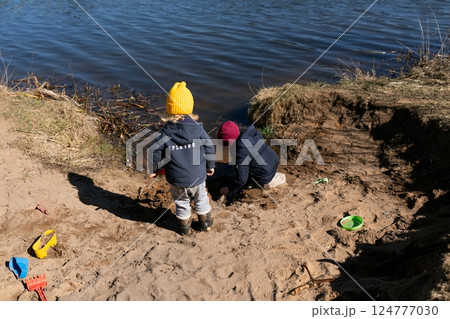 Children enjoy playtime by the riverbank, building sand structures during a sunny afternoon in early 124777030