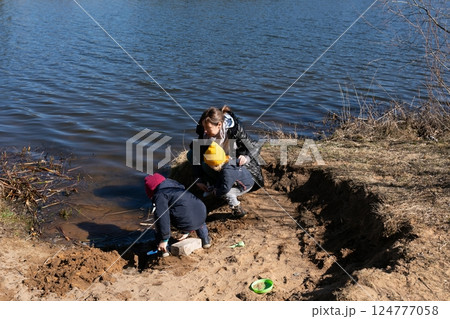 Children play by the riverbank while an adult supervises on a sunny day in early spring 124777058