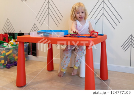 Child engages in creative play at a colorful table inside a bright room during the day 124777109