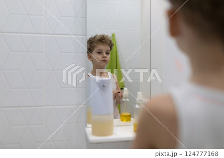 Young boy gazes thoughtfully at his reflection in bathroom mirror during morning routine Young boy gazes thoughtfully at his reflection in bathroom mirror during morning routine 124777168