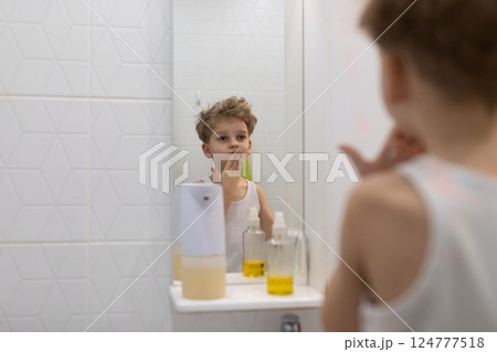 Child explores skin care routine in bathroom mirror reflection during morning hours Child explores skin care routine in bathroom mirror reflection during morning hours 124777518