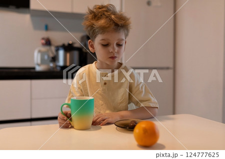 Young boy enjoying breakfast with a cup and fruit in a bright kitchen during morning hours Young boy enjoying breakfast with a cup and fruit in a bright kitchen during morning hours 124777625