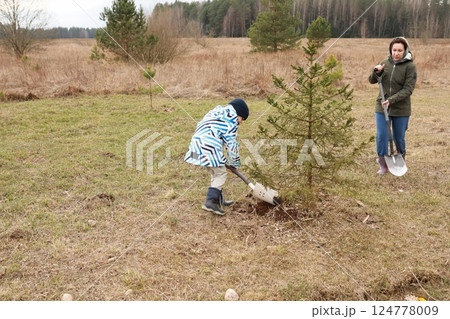 Children participate in tree planting activity in a grassy field during a cool afternoon in 124778009