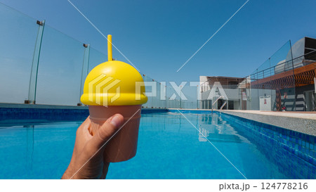 Hand holding refreshing iced drink by the rooftop pool on summer day 124778216