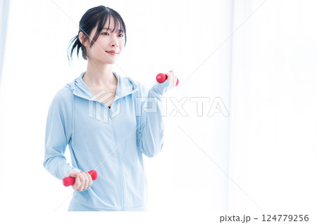 明るい部屋でダンベルトレーニングをする若い女性 明るい部屋でダンベルトレーニングをする若い女性 124779256