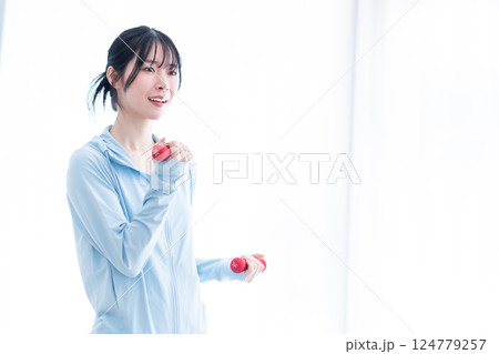 明るい部屋でダンベルトレーニングをする若い女性 明るい部屋でダンベルトレーニングをする若い女性 124779257