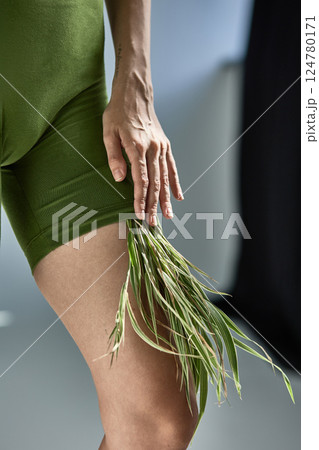 Person in green outfit with grass details touching leg gracefully, nature and fashion fusion concept 124780171