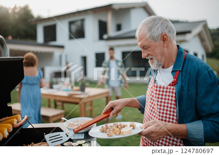 Senior man grilling food for a spring family weekend barbecue. 124780697