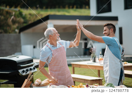 Father-in-law and son-in-law preparing food for a family barbecue. 124780778