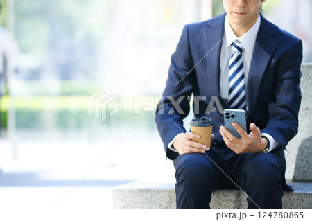 ビジネス街で座ってスマホを見るスーツの若い男性 ビジネス街で座ってスマホを見るスーツの若い男性 124780865