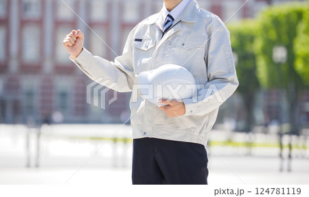 ヘルメットを抱えガッツポーズをする作業服の若い男性 124781119