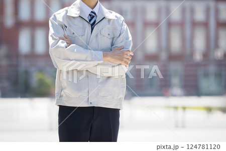 建設現場を背に腕組みをして立つ作業服の男性 124781120
