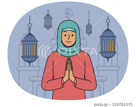 Muslim woman in hijab makes prayer gesture standing near mosque and traditional islamic lanterns 124781335