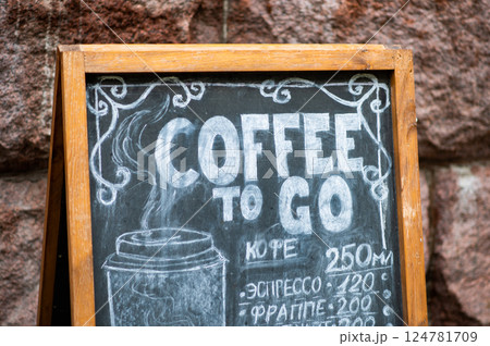 An advertisement for takeaway coffee painted in white chalk on a dark board. 124781709