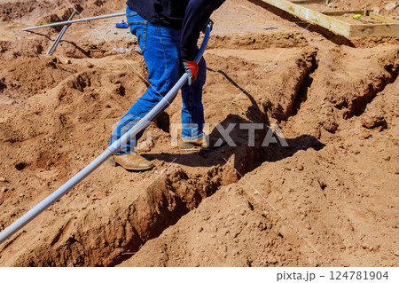 Worker laying out electrical pvc pipes in trench dirt at construction site during foundation work 124781904
