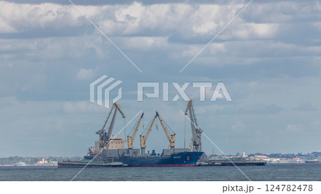 Loading and unloading a Cargo freight ship with industrial cranes in the middle of river timelapse. 124782478