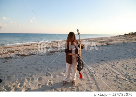 Girl Plays Bass Music Instrument On The Beach At Sunset Near Ocean Girl Plays Bass Music Instrument On The Beach At Sunset Near Ocean 124783076