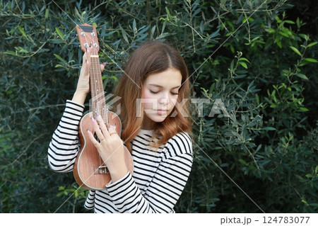Artist Girl Plays Ukulele Musical Instrument Outside In Park Near A Tree Artist Girl Plays Ukulele Musical Instrument Outside In Park Near A Tree 124783077