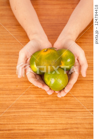 Young Caucasian male holding yellow and green tangerines in hand over brown wooden table Young Caucasian male holding yellow and green tangerines in hand over brown wooden table 124784418