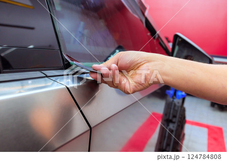 Worker carefully applies protective film to car window while working in an auto detailing shop 124784808