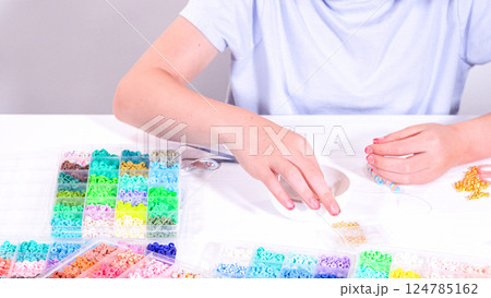 Delicate fingers of a young girl navigate through a treasure trove of bright, multicolored beads, each compartment revealing a new hue to choose from. 124785162