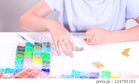 Delicate fingers of a young girl navigate through a treasure trove of bright, multicolored beads, each compartment revealing a new hue to choose from. 124785163