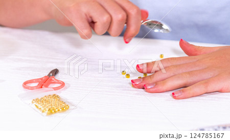 Delicate fingers of a young girl navigate through a treasure trove of bright, multicolored beads, each compartment revealing a new hue to choose from. She's immersed in the joyful task of stringing 124785167