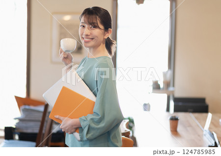 ノートパソコンを持ちながら立ってコーヒーを飲む女性 124785985