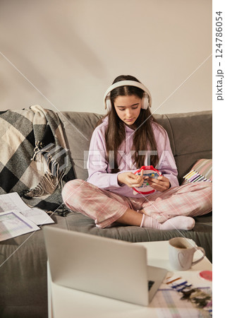 Teen girl wearing headphones and doing embroidery with colorful threads, learning handcraft skills during creative online session. Teen girl wearing headphones and doing embroidery with colorful threads, learning handcraft skills during creative online session. 124786054