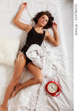 Sexy lazy girl lying with red alarm clock on bed Sexy lazy girl lying with red alarm clock on bed 124786722