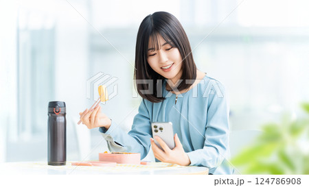 スマートフォンを見ながらお弁当を食べる女性・ビジネスウーマン 124786908