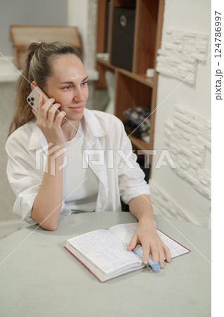Close up of a woman hands checking smart phone calendar and writing on agenda t at home Close up of a woman hands checking smart phone calendar and writing on agenda t at home 124786997