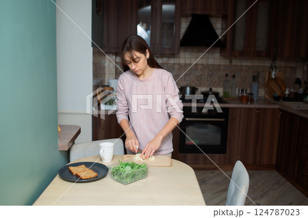 Woman slicing artisan cheese on wooden board, preparing fresh breakfast healthy food with crisp corn salad and whole wheat toast in sunlit kitchen 124787023