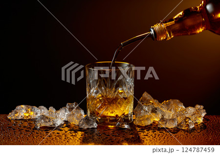 Whiskey pours from bottle to glass. 124787459