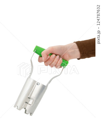Hand holding a bulb planter tool with a green handle, isolated on white background. 124787632