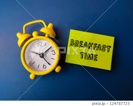 Alarm clock and sticky note with the word BREAKFAST TIME on blue background. Alarm clock and sticky note with the word BREAKFAST TIME on blue background. 124787723