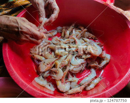 Closeup the shrimp in the red container are being peeled to be cooked. 124787750