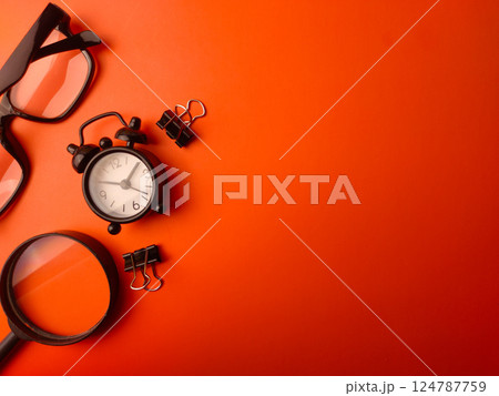 Top view magnifying glass,clock,paper clips and glasses on a orange background with copy space. Business concept. 124787759